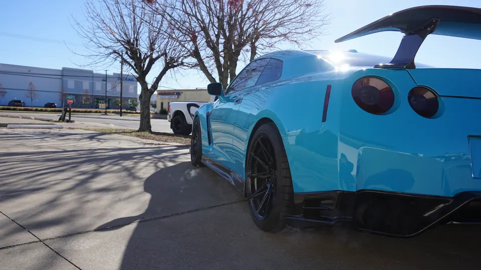 Bright blue Nissan GT-R with a large aftermarket rear wing and diffuser parked outdoors on a sunny day.