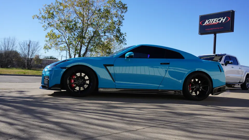 Blue Nissan GT-R parked outside Jotech Motorsports performance tuning shop on a sunny day.