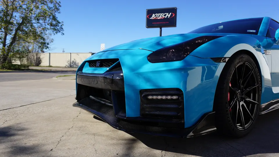A blue Nissan GT-R with carbon fiber front splitter and aftermarket wheels parked outside Jotech Motorsports.