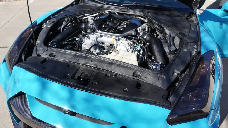 A Nissan GT-R engine bay with custom black intake piping and a blow-off valve, showcasing performance upgrades.