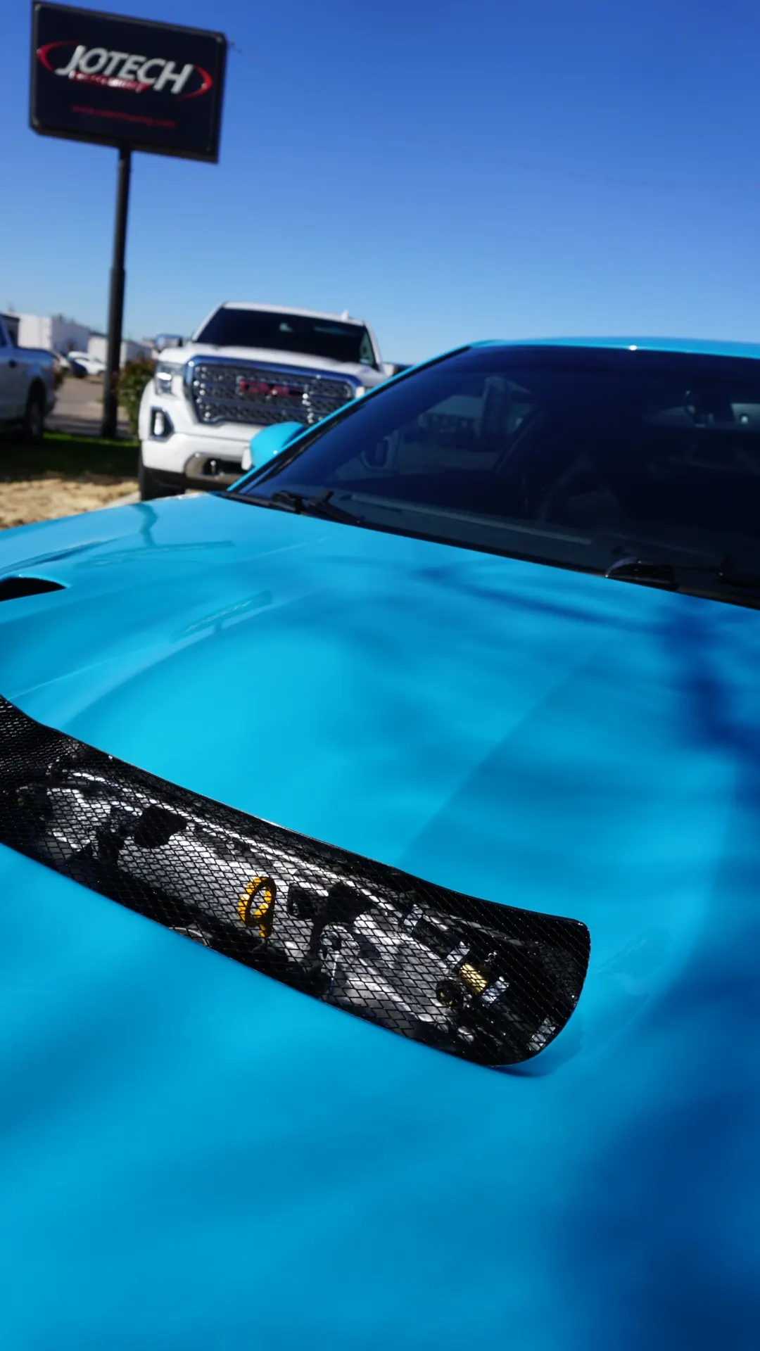 Close-up of a bright blue sports car's hood with a black mesh vent, parked outside Jotech Technology.