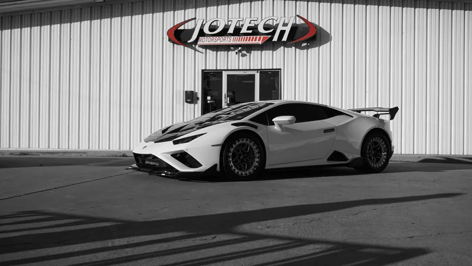 White Lamborghini Huracan with aftermarket wheels and a large rear wing parked in front of Jotech Motorsports.