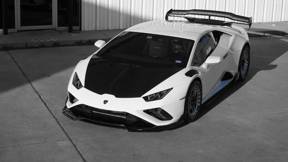 White Lamborghini Huracan with a black carbon fiber hood, front splitter, and large rear wing parked outside.