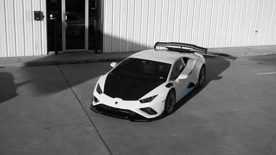 White Lamborghini Huracan with a black carbon fiber hood, large rear wing, and front splitter parked outside a building.
