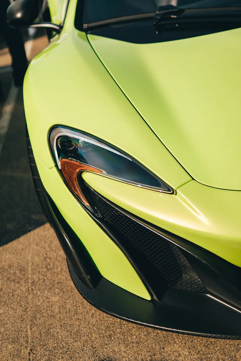 A close-up detail shot of the bright green McLaren's front headlight and carbon fiber bumper.