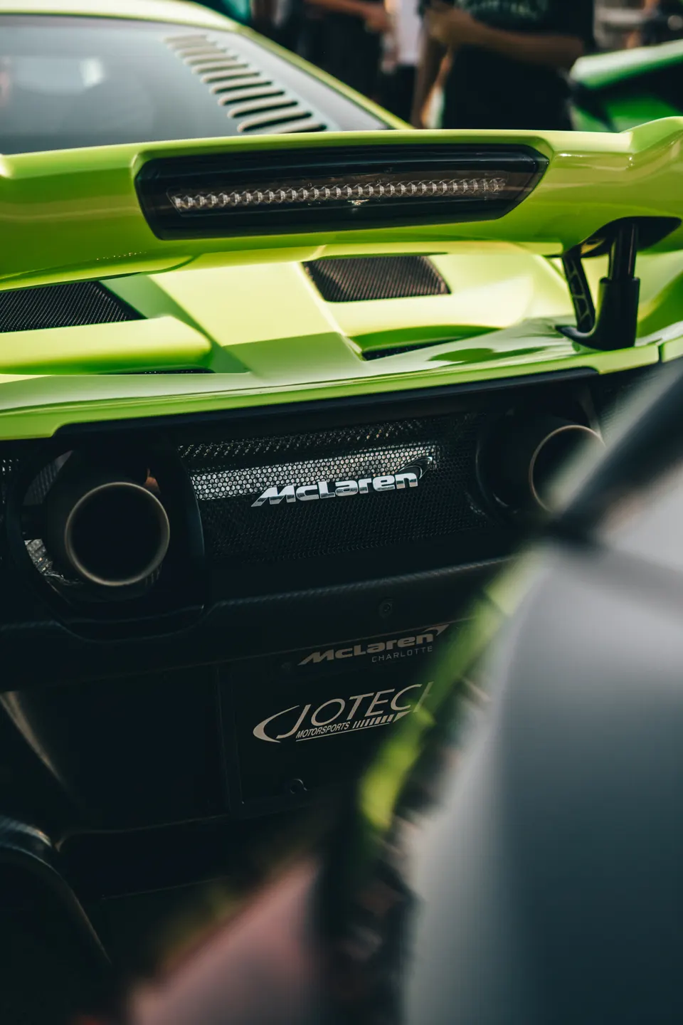 Rear detail of a lime green McLaren supercar, showing exhaust tips, carbon fiber grille, and active rear wing.