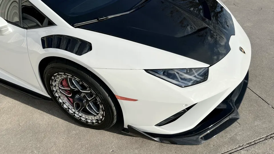 A white Lamborghini Huracan with a carbon fiber hood, fender vents, and drag racing wheels.