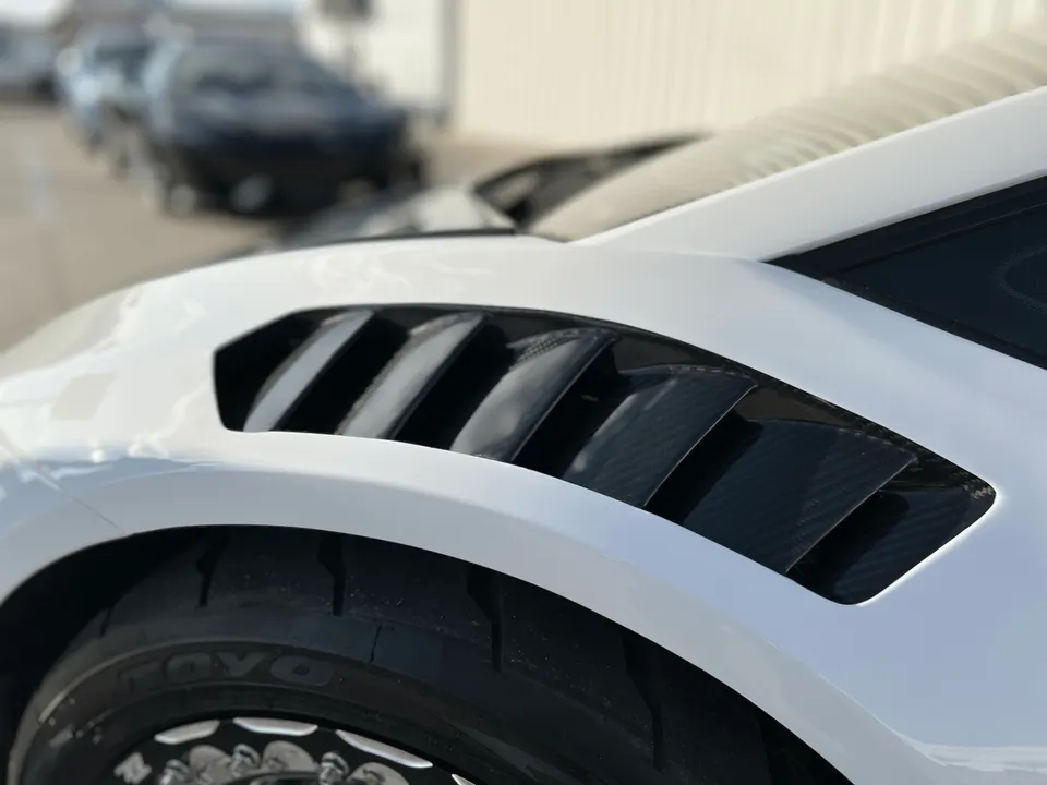 A close-up of a white car's fender with carbon fiber vents and a Toyo tire on an aftermarket wheel.