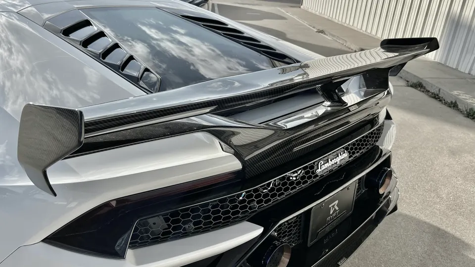 White Lamborghini supercar with a prominent carbon fiber rear wing, engine cover, and exhaust system.