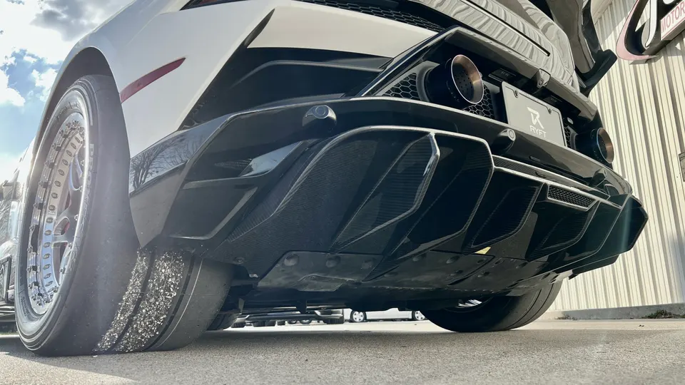 Low-angle rear view of a white Lamborghini with a carbon fiber diffuser, large exhaust tips, and wide drag tires.