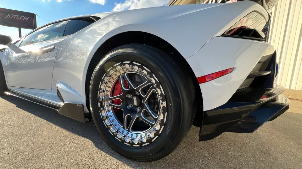 A white Lamborghini Huracan with aftermarket drag wheels, carbon fiber side skirts, and a rear diffuser.
