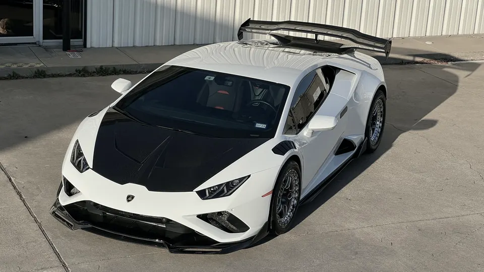 White Lamborghini Huracan with a black carbon fiber hood and large aftermarket rear wing parked outdoors.