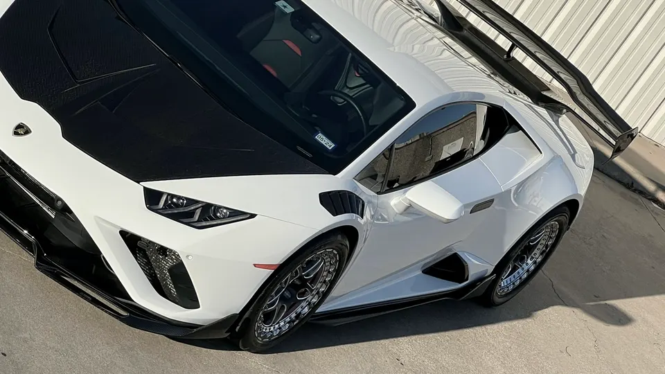 A white Lamborghini Huracan with a black carbon fiber hood, custom wheels, and a large rear wing parked outdoors.