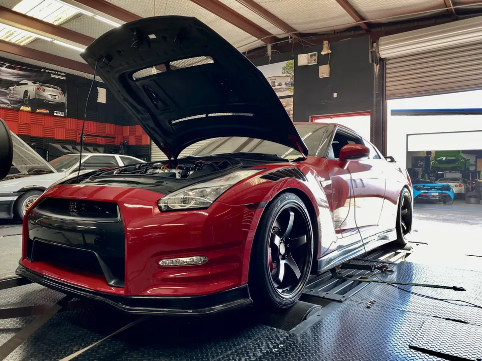 Red Nissan GT-R with its hood open strapped to a dyno in a performance tuning shop