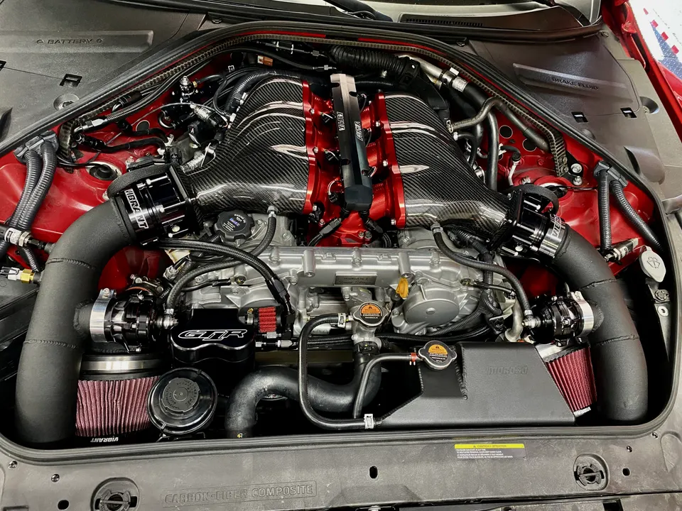 Highly modified Nissan GT-R R35 engine bay featuring a carbon fiber intake manifold, Vibrant blow-off valves, and custom components.