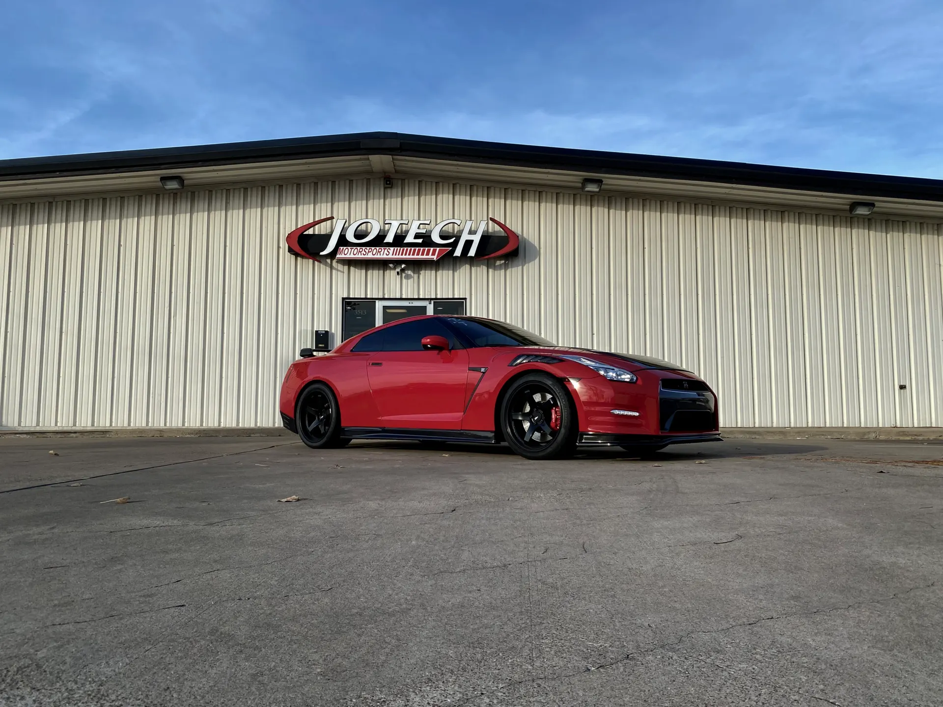 Red Nissan GT-R parked in front of Jotech Motorsports performance shop on a sunny day.