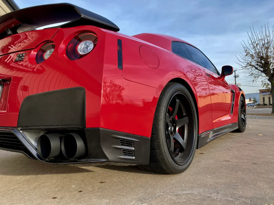 A red Nissan GT-R with aftermarket wheels and a carbon fiber rear diffuser, showcasing its aftermarket exhaust system.