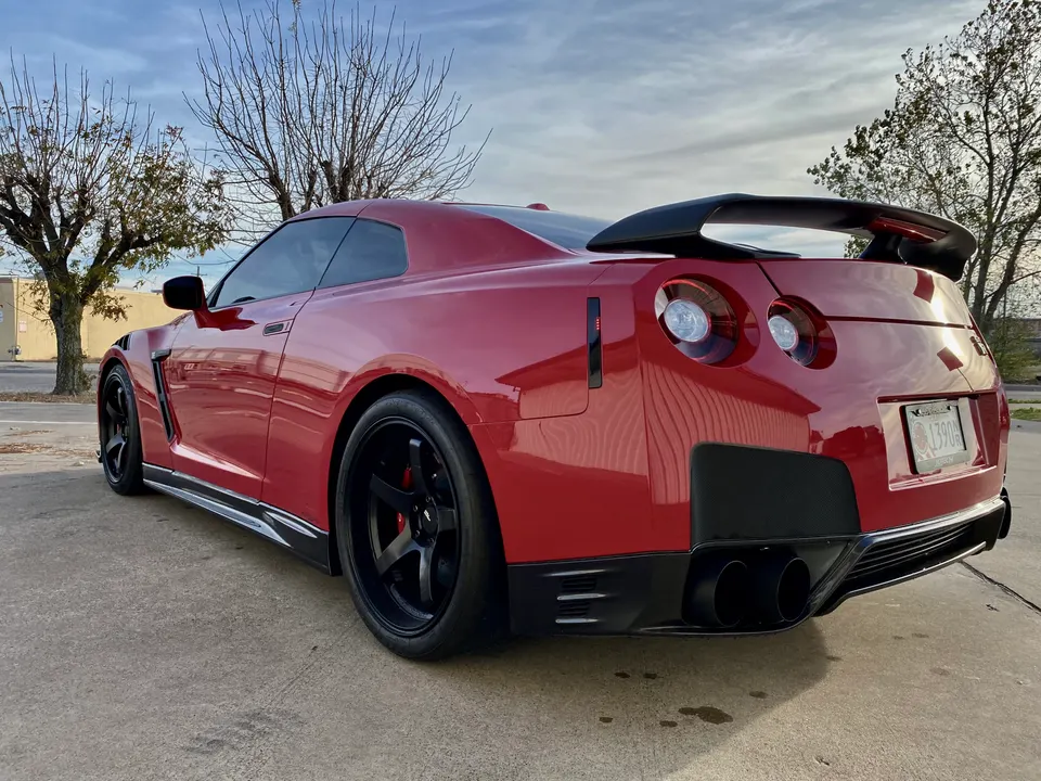 Red Nissan GT-R with aftermarket wheels, large rear wing, and custom exhaust system parked outdoors.