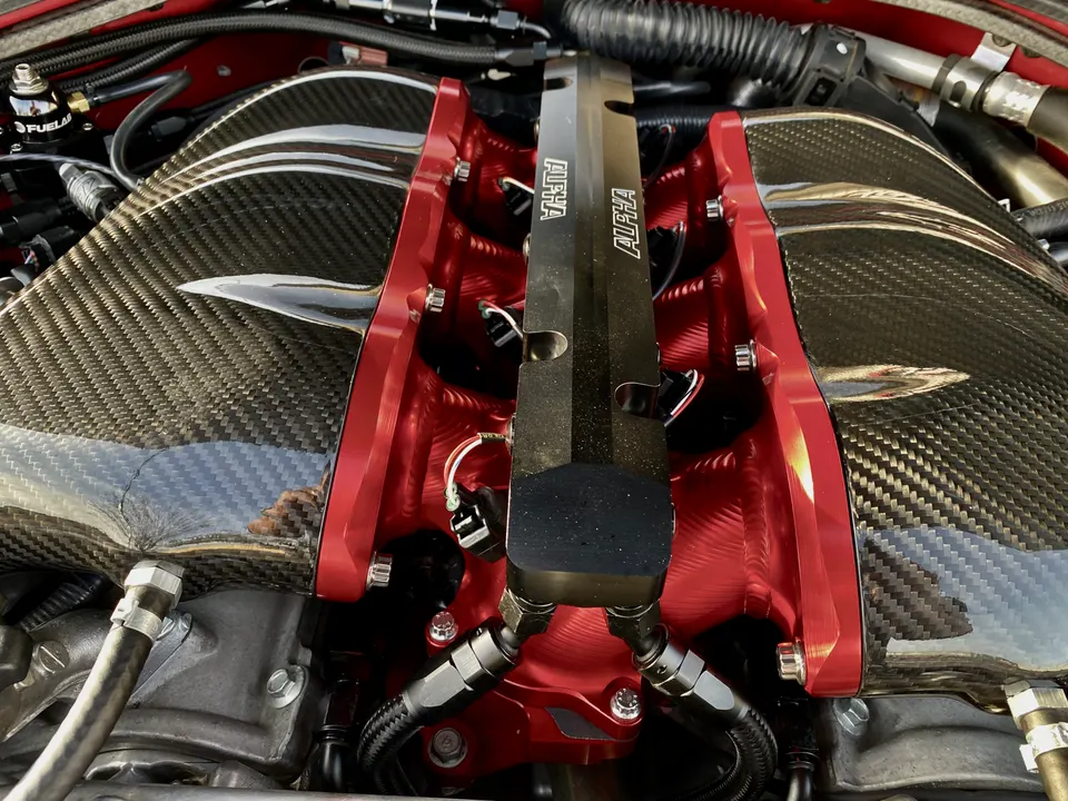 A close-up of a custom carbon fiber intake manifold and red billet fuel rails in a high-performance engine bay.