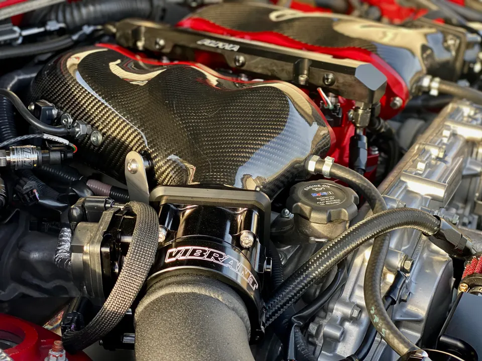 Close-up of a high-performance engine bay featuring a carbon fiber intake manifold and Vibrant Performance throttle body.