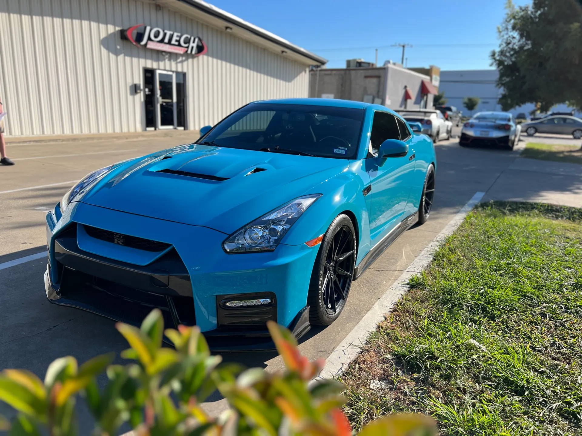 Blue Nissan GT-R with aftermarket wheels and front splitter parked outside Jotech Motorsports performance shop.