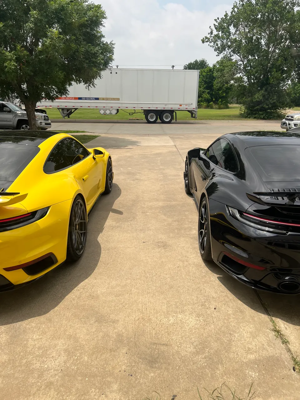 Two Porsche 911 sports cars, one yellow and one black, parked outdoors on a sunny day.