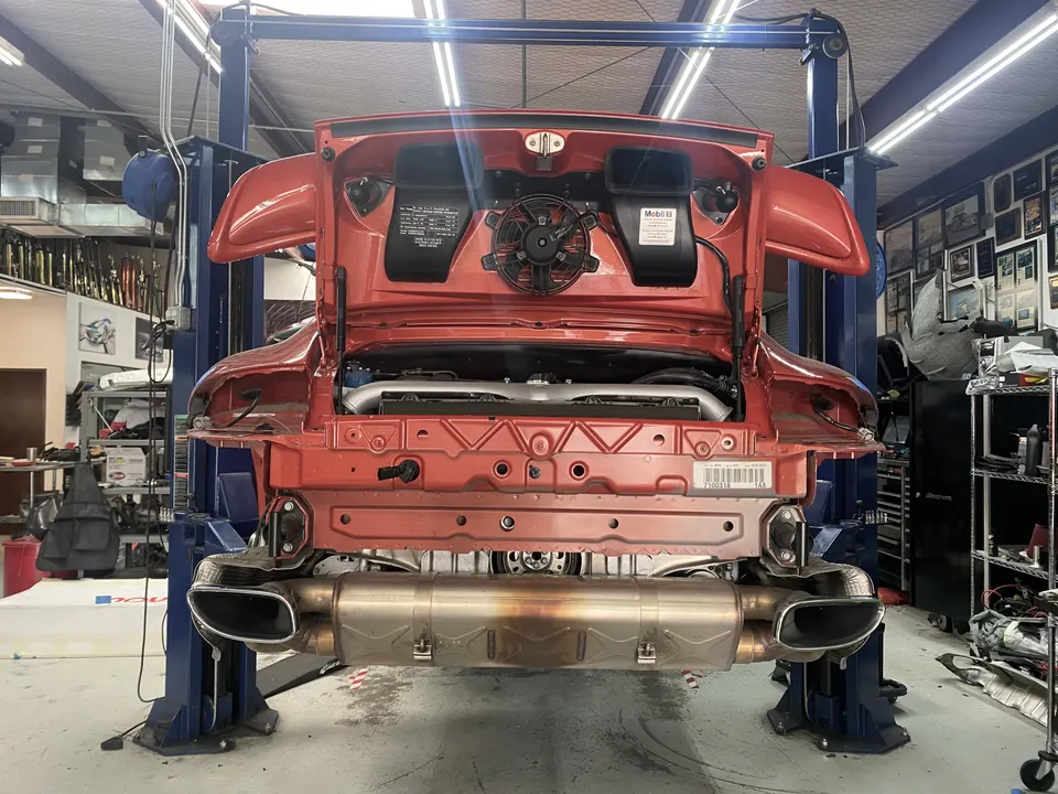 Rear view of a red Porsche 911 on a lift in a performance shop, with its exhaust system exposed.