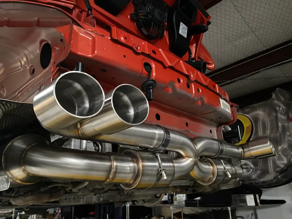 Custom stainless steel exhaust system installed on the underside of a red sports car in a performance shop.