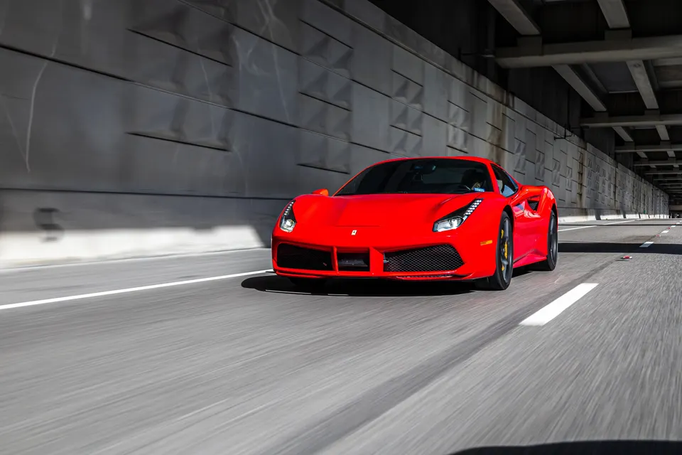 A vibrant red Ferrari 488 sports car drives on a highway under an overpass, captured in a dynamic roller shot.