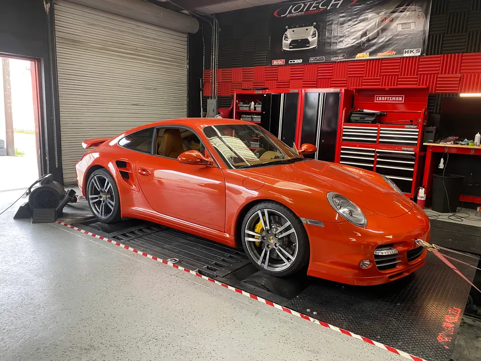 An orange Porsche 911 Turbo strapped to a dynamometer at Jotech Motorsports for performance tuning.