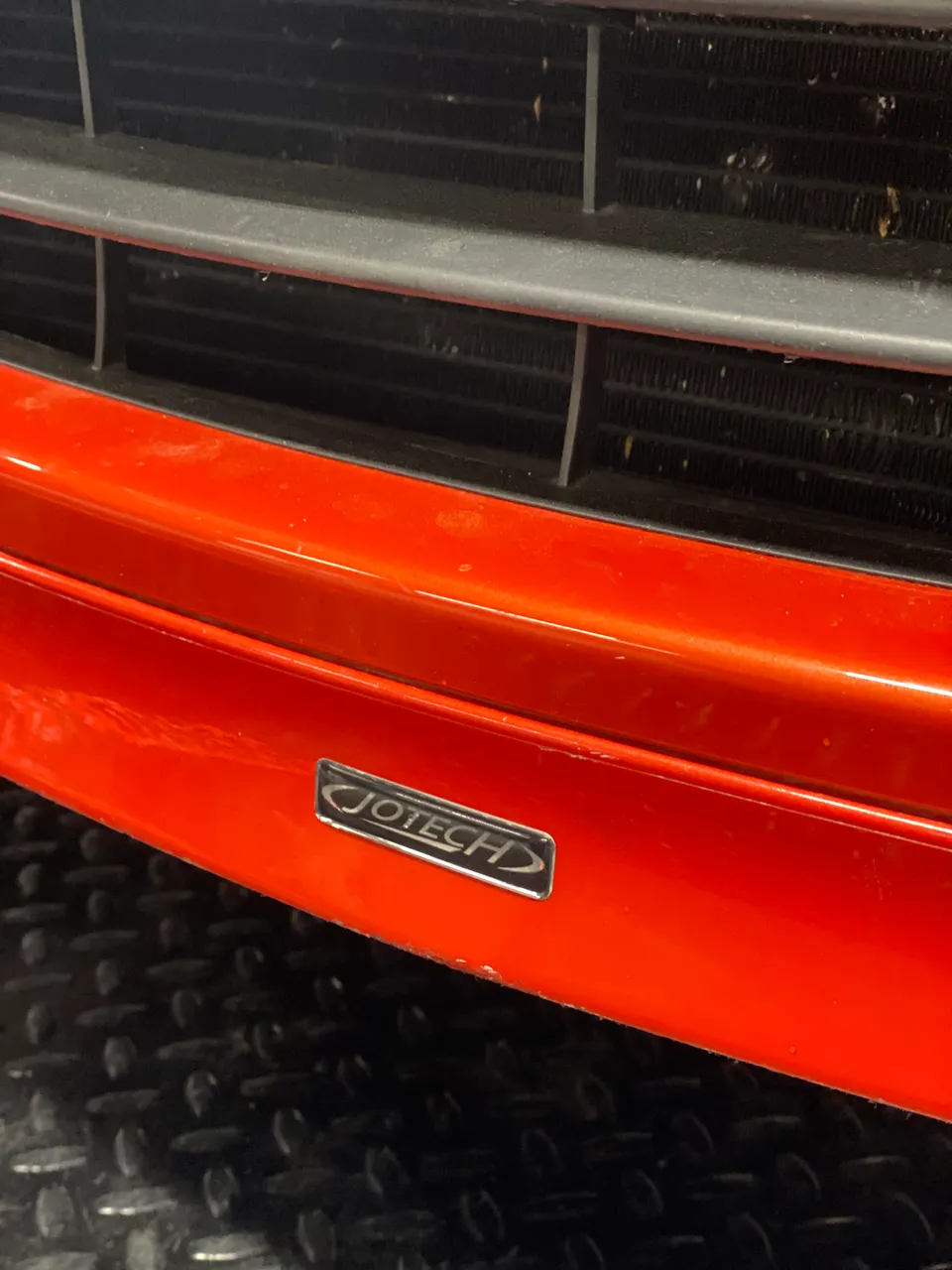 Close-up of a red car's front bumper featuring a Jotech badge and part of the grille.