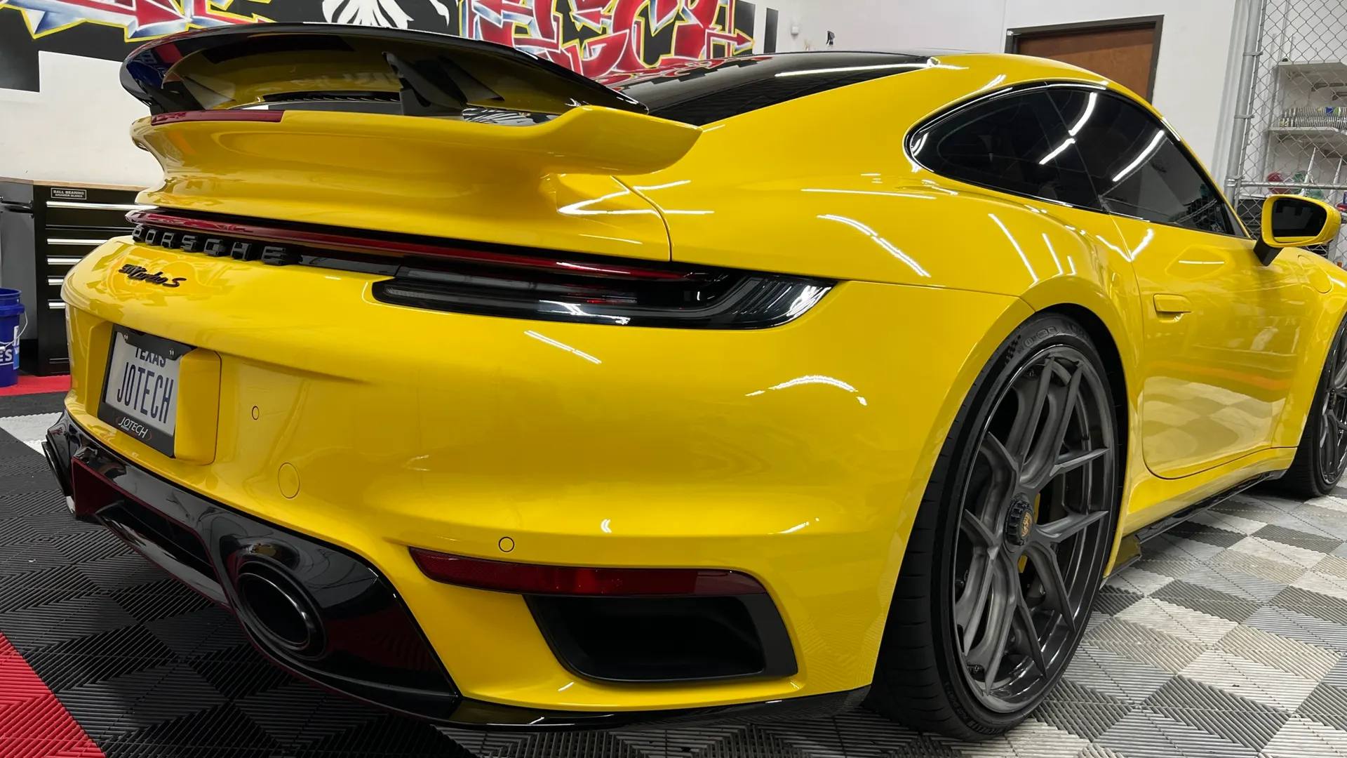Yellow Porsche 911 Turbo S with a prominent rear wing and custom wheels, parked in a clean shop environment.