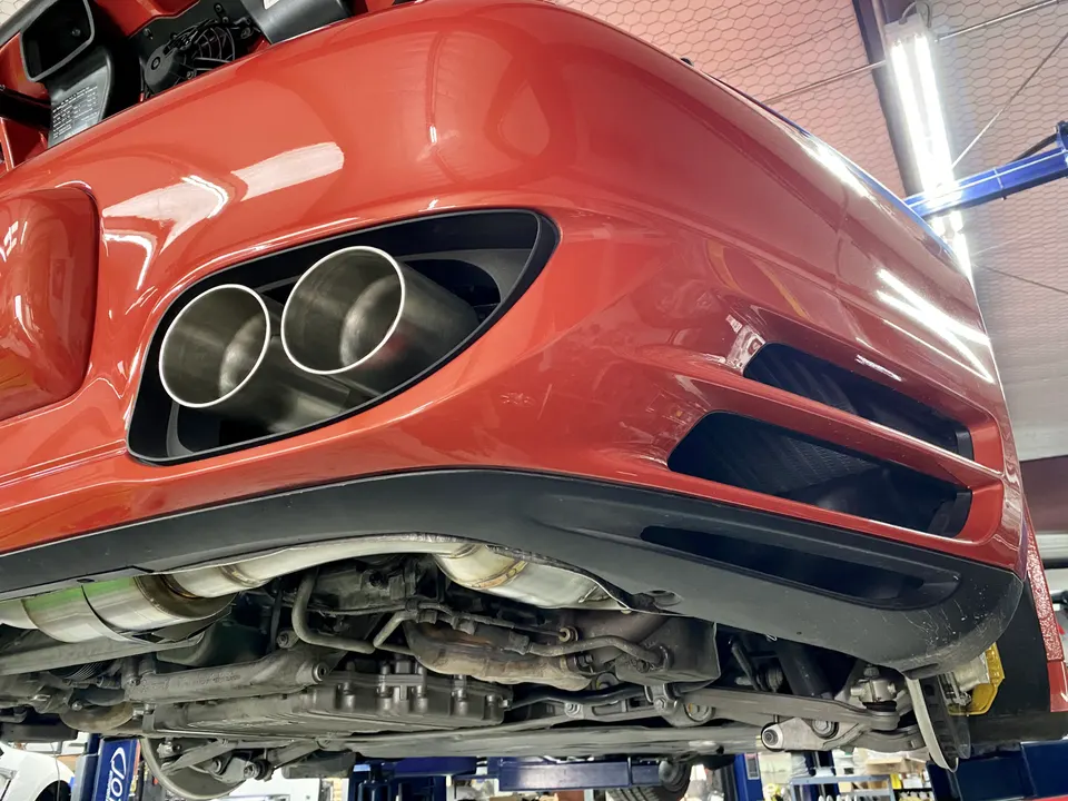 Rear underside view of a red Porsche on a lift, showcasing the aftermarket exhaust system with dual tips.
