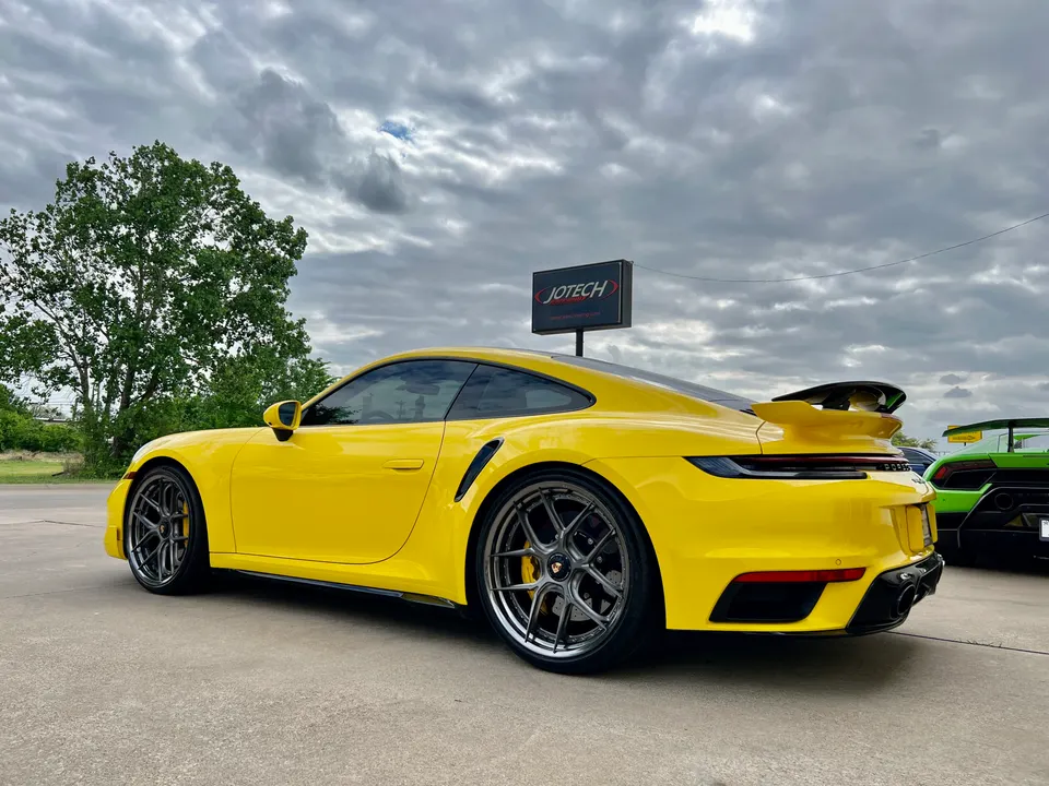 Yellow Porsche 911 Turbo S with custom wheels and a rear wing parked outside Jotech Motorsports.
