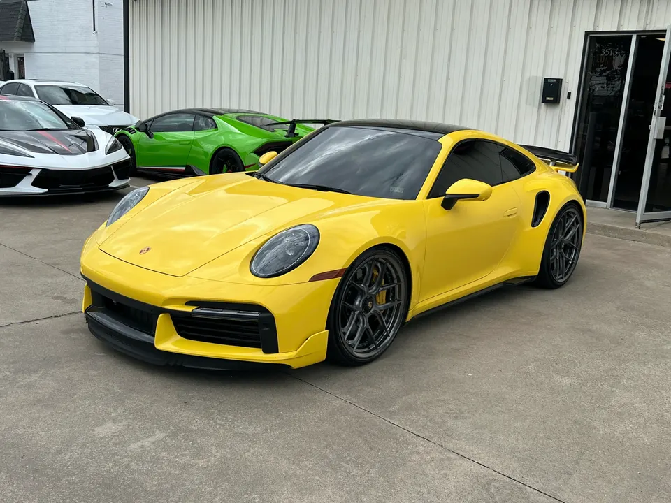 A bright yellow Porsche 911 with black roof and aftermarket wheels parked outside a performance shop.
