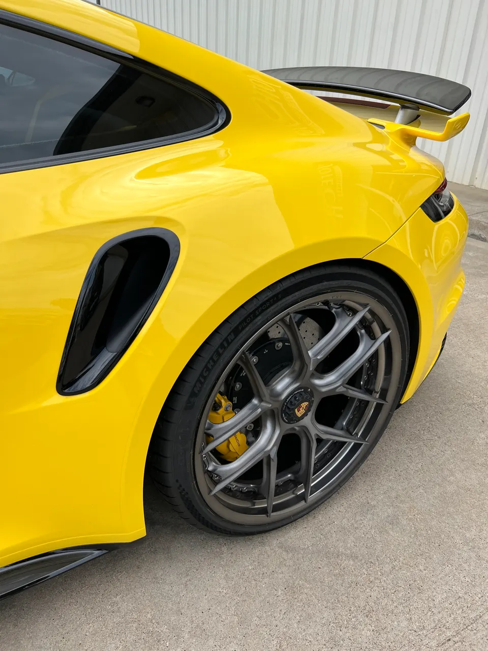 Close-up of a yellow Porsche 911 GT3 RS rear quarter, highlighting the grey multi-spoke wheel, yellow brake calipers, and carbon fiber wing.