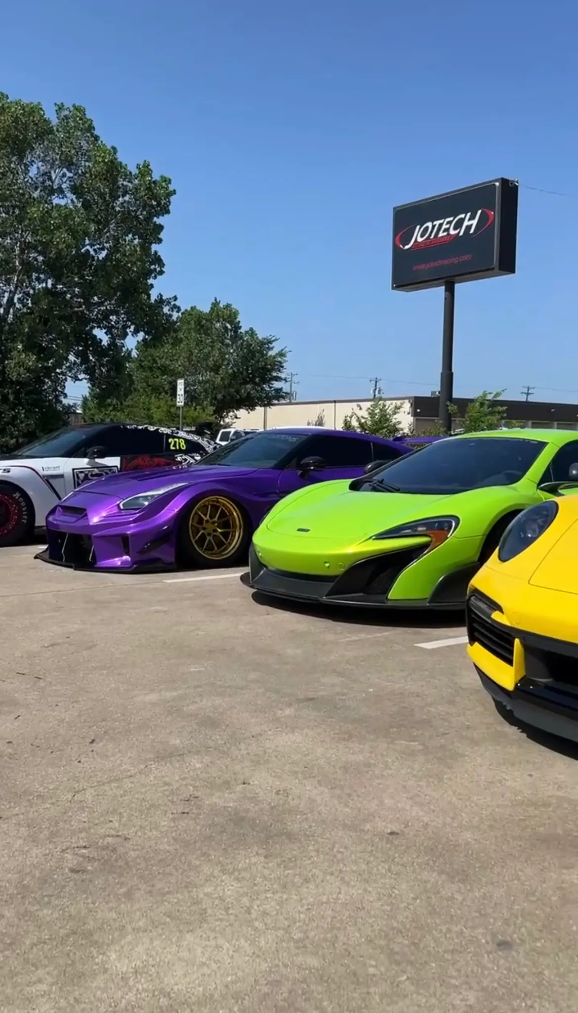 A line of custom supercars including a purple Nissan GT-R, a lime green McLaren, and a yellow Porsche parked outside Jotech Motorsports.