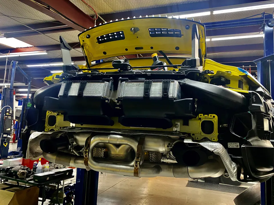 A yellow Porsche 911 on a lift in a shop with its rear bumper removed, showcasing a Soul Performance exhaust system.