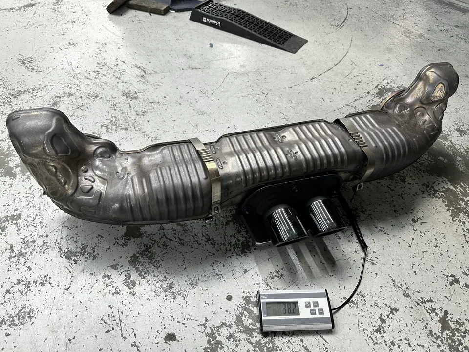 Aftermarket exhaust system with dual tips being weighed on a digital scale on a shop floor.