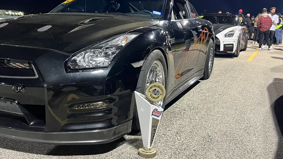 Black Nissan GT-R drag car with a carbon fiber hood and a trophy at a night track event.