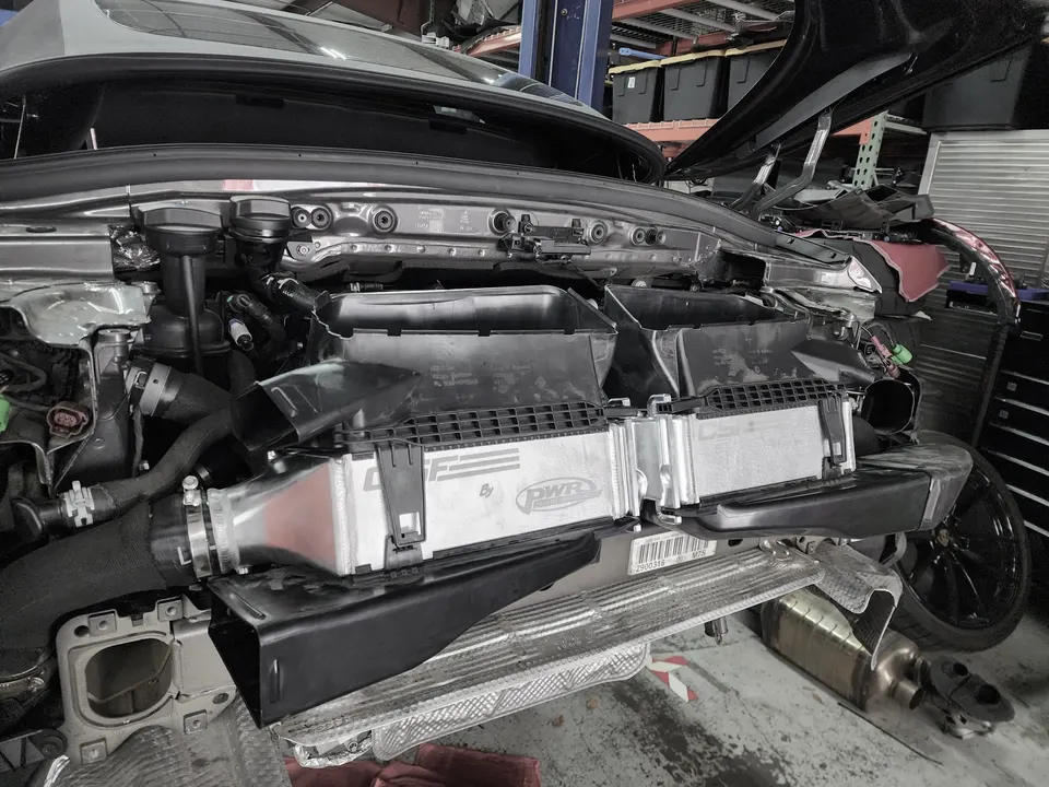 A car in a shop with its front bumper removed, showcasing a PWR performance intercooler installation.