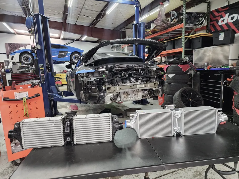 Audi R8 undergoing performance upgrades in a tuning shop, with new intercoolers on a table ready for installation.