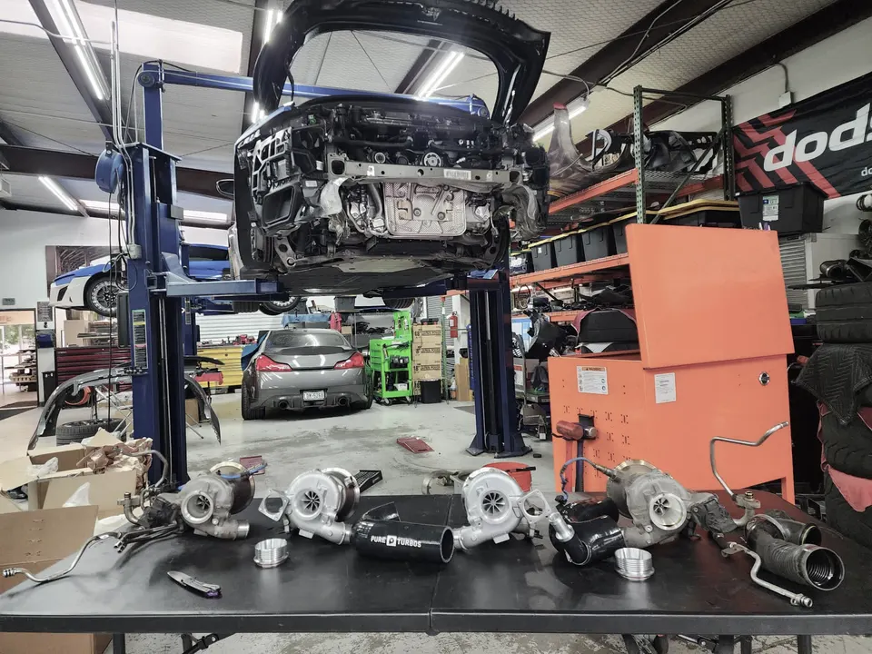 A car on a lift in a performance shop with multiple turbochargers and tuning parts laid out on a table.