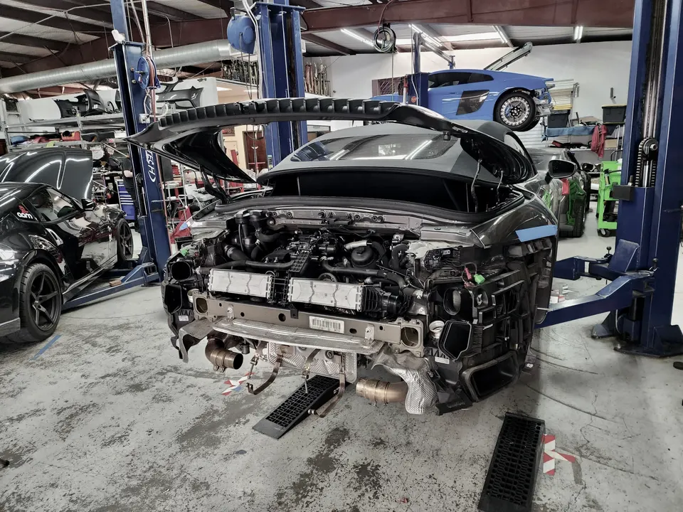 A Lamborghini Huracan undergoing disassembly in a performance tuning shop, with its front bumper removed exposing the engine and cooling system.