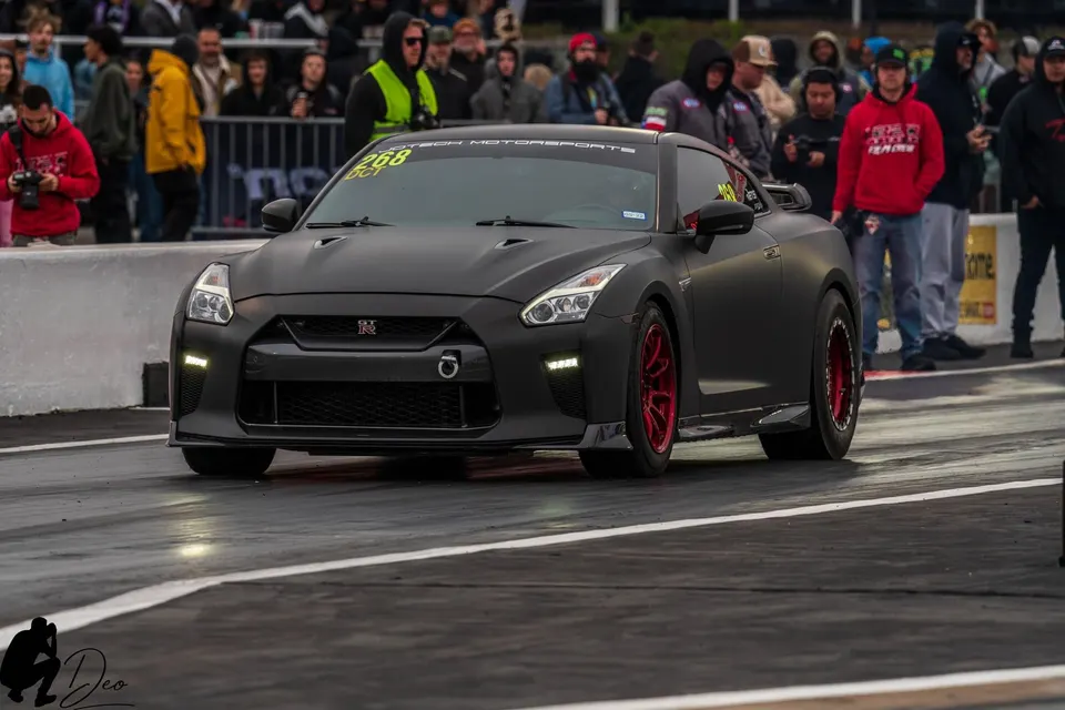 Matte black Nissan GT-R with red wheels on a drag strip, featuring a Jotech Motorsports banner.