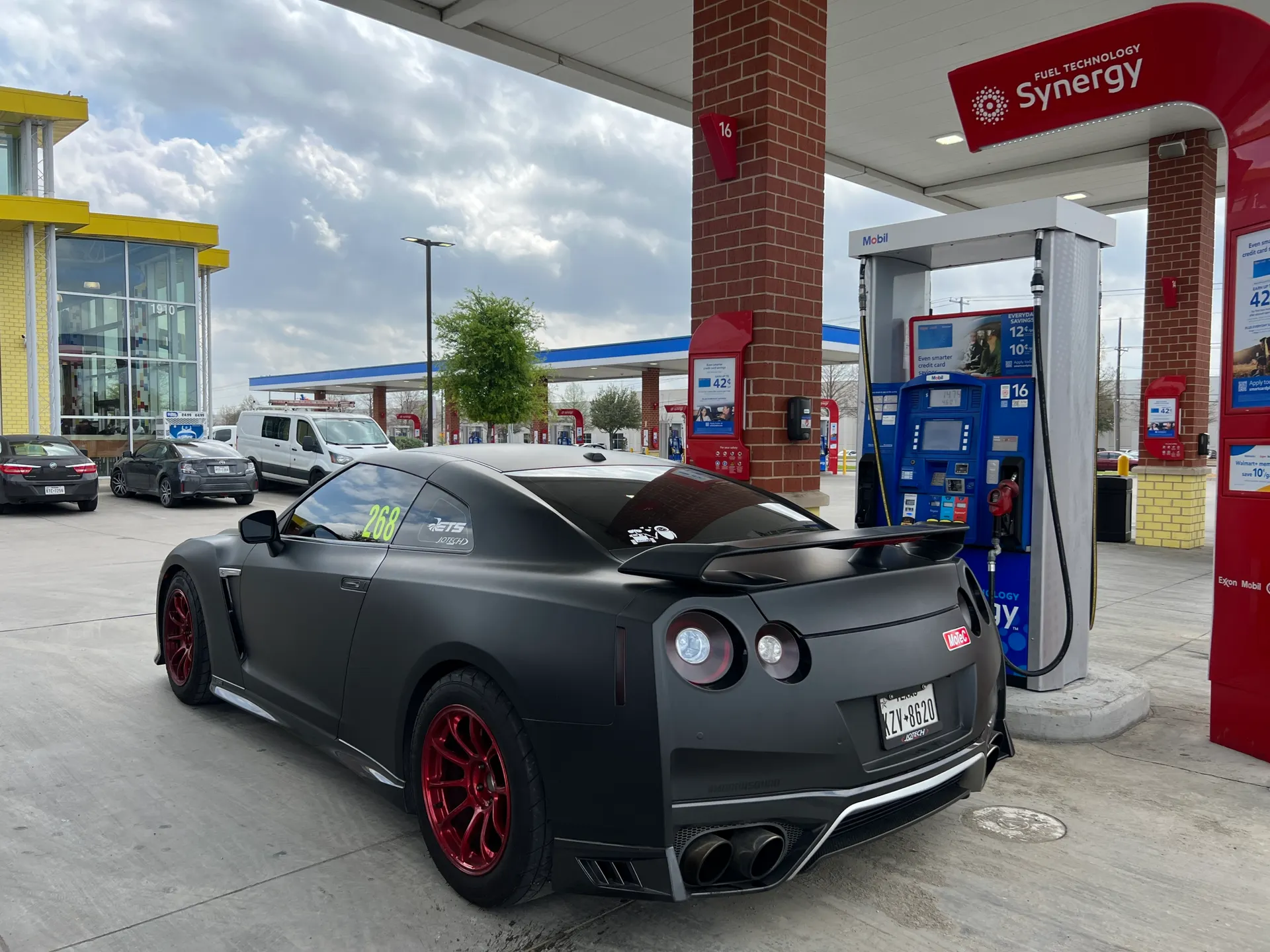 A matte black Nissan GT-R with red wheels at a gas station.