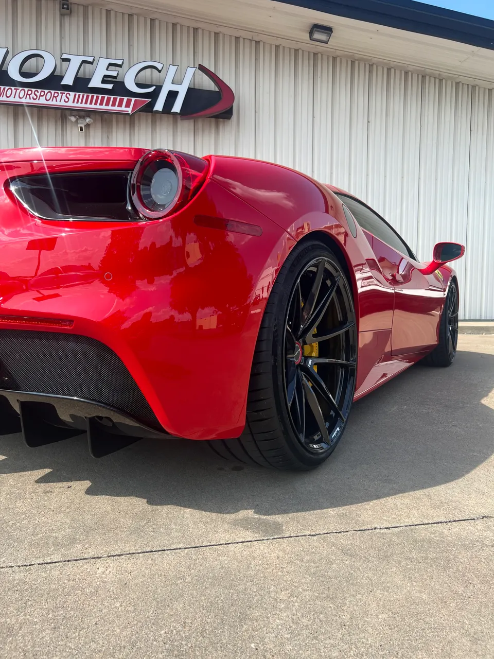 Red Ferrari 488 parked outside Jotech Motorsports, showcasing custom black wheels with yellow calipers and a carbon fiber rear diffuser.