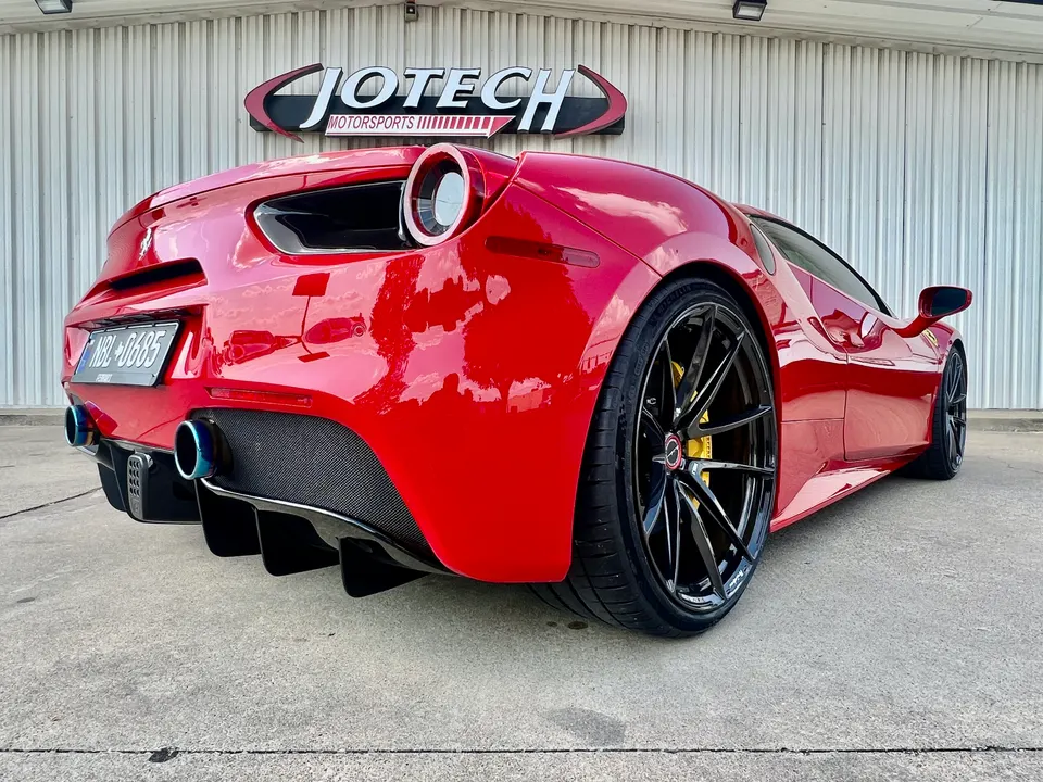 A red Ferrari 488 with custom black wheels, a carbon fiber rear diffuser, and aftermarket exhaust tips parked at Jotech Motorsports.