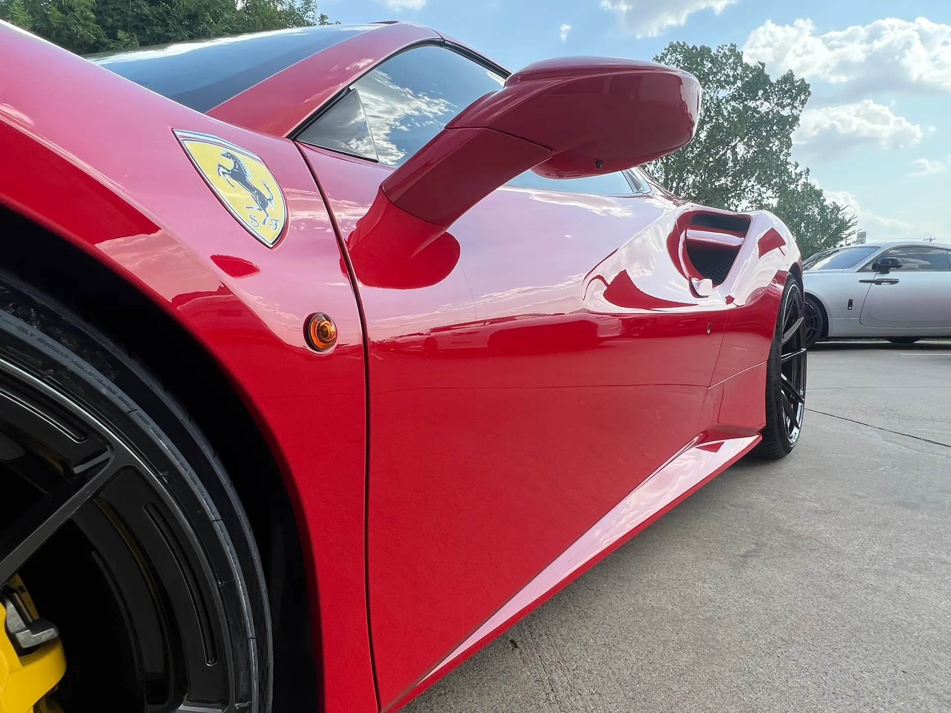 Red Ferrari sports car side profile with black multi-spoke wheels and yellow brake calipers parked outdoors.