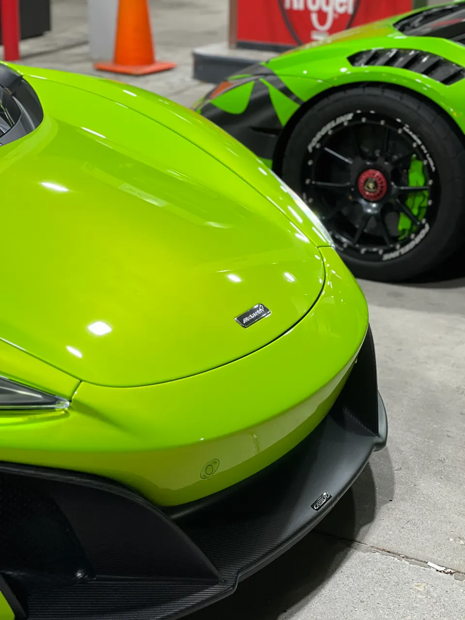 Close-up of a bright green McLaren supercar's front end with a carbon fiber splitter, parked next to another green supercar.
